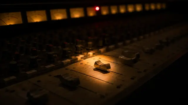 A mixing console channel strip in warm light with a single red clip light glowing on the meter bridge