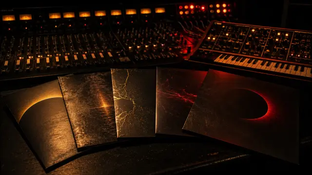 Five matte black record sleeves with gold and crimson accents fanned across a dark console desk beside a synthesizer and mixing console