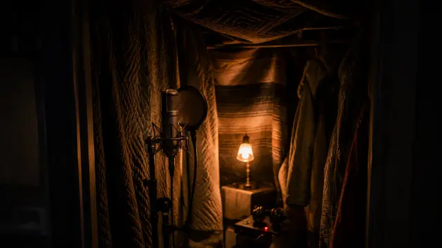 A microphone inside a makeshift vocal booth of hanging blankets and coats, lit by a small warm lamp